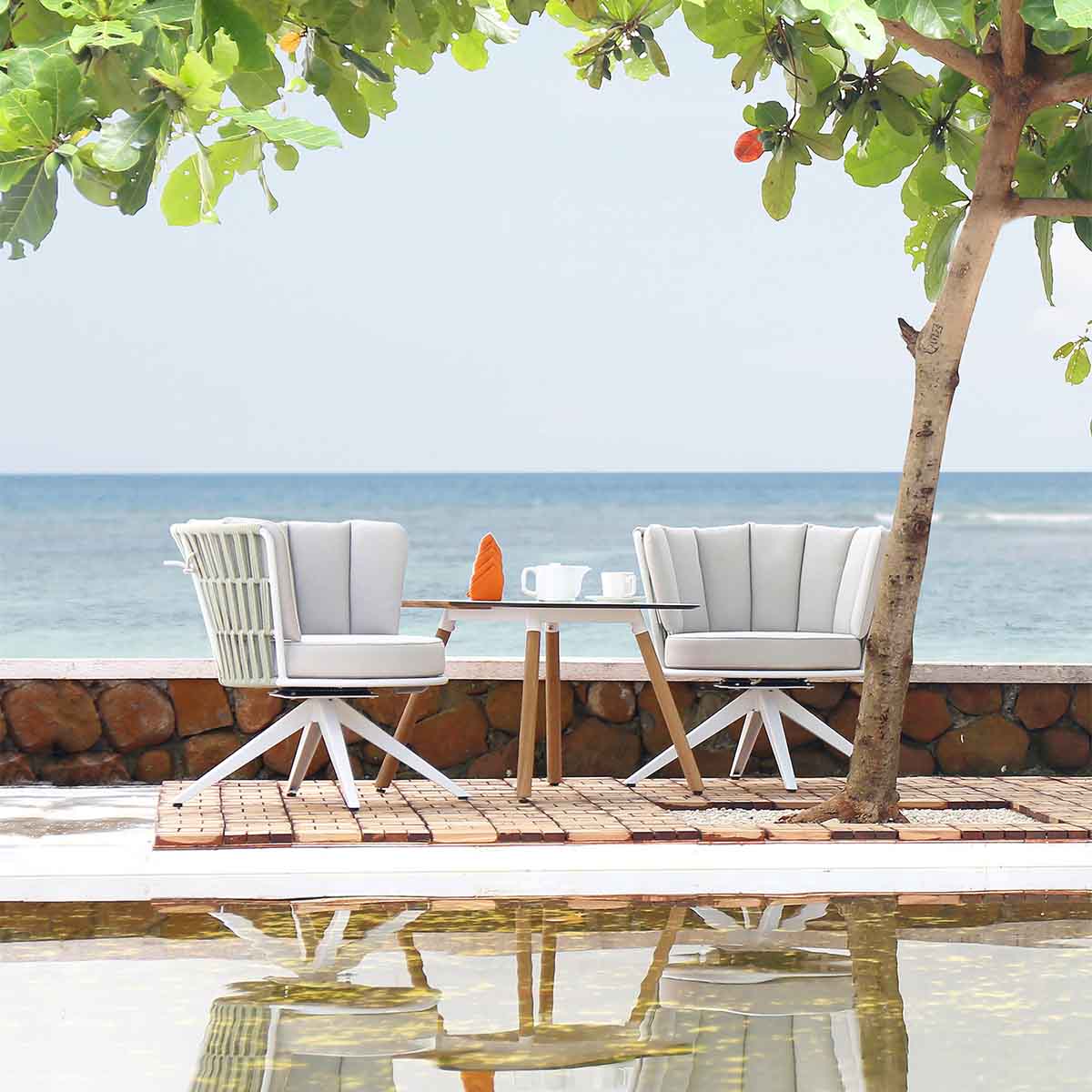 commercial outdoor low table with two cushioned swivel chairs by a pond and the ocean